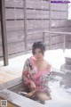 A woman in a pink kimono sitting in a hot tub.