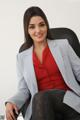 A woman sitting in a chair wearing a gray blazer and red top.