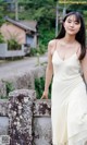 A woman in a white dress leaning against a stone wall.