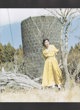 A woman in a yellow dress leaning against a tree.