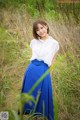 A woman in a white shirt and blue skirt standing in tall grass.