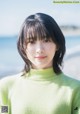 A woman in a green sweater standing on a beach.