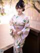 A woman in a pink kimono standing next to a tree.