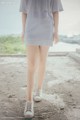 A woman in a gray dress is walking on a dirt road.