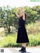 A woman in a black dress and black boots standing on a sidewalk.