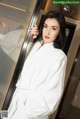 A woman in a white robe leaning against a glass door.